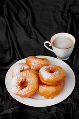 donuts with powdered sugar and coffee on a black background