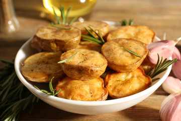 Delicious baked potato with rosemary in bowl on table close up