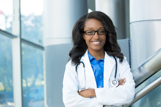 Closeup portrait of friendly, smiling confident female healthcare professional with lab coat, stethoscope, arms crossed. Isolated hospital clinic background. Time for an office visit