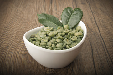 White bowl with green coffee beans on the wood