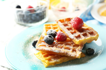 Sweet homemade waffles with forest berries on plate, on light background