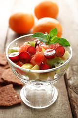 Fruit salad in glass bowl, on wooden background