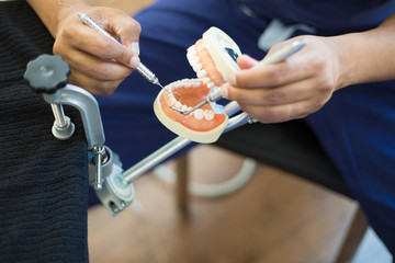 Closeup portrait, young oral professional student practicing dental procedures on plastic teeth, wax typodont mounted on table. Drilling cavity preparations and filling with restorative materials