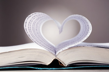 Book pages curved into heart shape on gray background