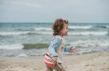 Little curly girl playing in the sand on seashore
