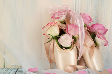 Bouquet of roses in ballet shoes on wooden background