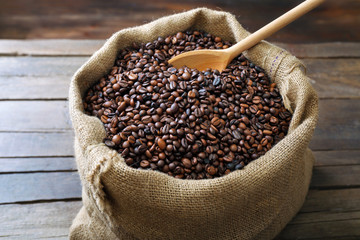 Sac with roasted coffee beans with spoon on wooden background
