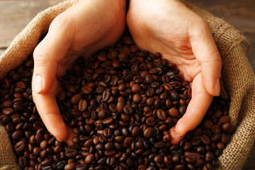 Hands in sac with roasted coffee beans on wooden table