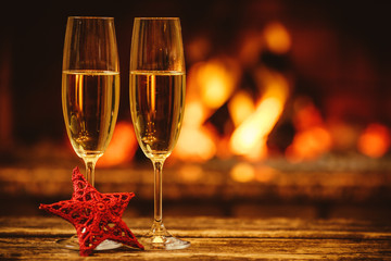Two glasses of sparkling champagne in front of warm fireplace. Cozy relaxed magical atmosphere in a...