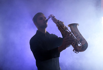 Obraz na płótnie Canvas Elegant saxophonist plays jazz in blue smoke