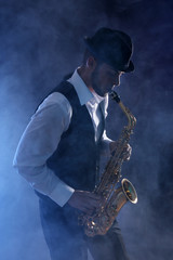 Obraz na płótnie Canvas Elegant saxophonist plays jazz on dark background in blue smoke