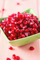 pomegranate seeds in a bowl on wooden surface