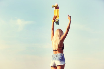 Young woman with skating board on blue sky background