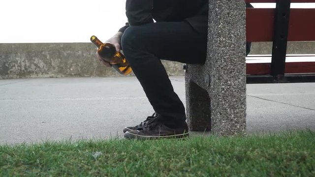 Man depressed with wine bottle sitting on bench outdoor 4K