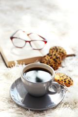 Cup of coffee with biscuits and book on carpet in room