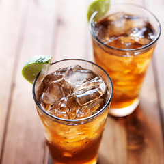 two glasses of iced tea with lime wedges on wooden table close up