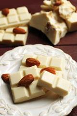 White chocolate pieces with nuts on plate, on color wooden background