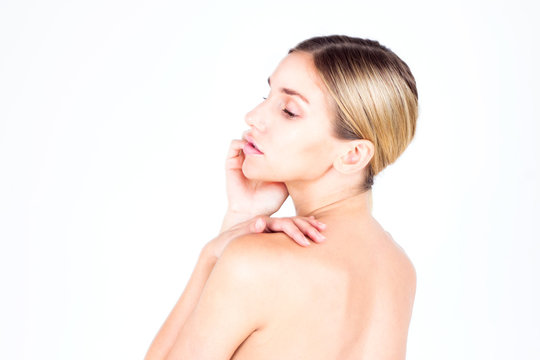Young woman with beautiful skin and a naked back looking down and touching her face. Beauty concept.