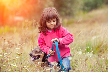 Happy little girl walking with dog on the meadow