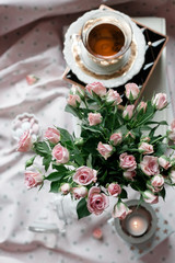 Bucn of pink roses set with a cup of tea and candles.