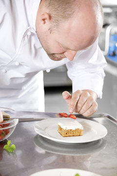 Chef decorates dessert cake with strawberry in kitchen