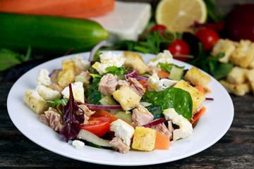 Tuna salad with Spinach, rocket, red ruby chard, tomatoes, cucumbers, white cheese, carrot, red onion, croutons, yellow lime on old wooden table background