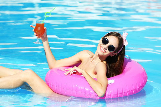 Young woman enjoying with rubber ring and cocktail in swimming pool at summertime