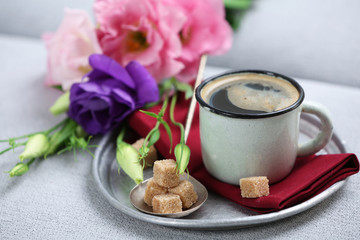 Cup of coffee with flowers on tray on sofa in room