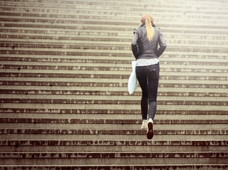 Young adult woman walks up the stairs (in the rain, into the light)