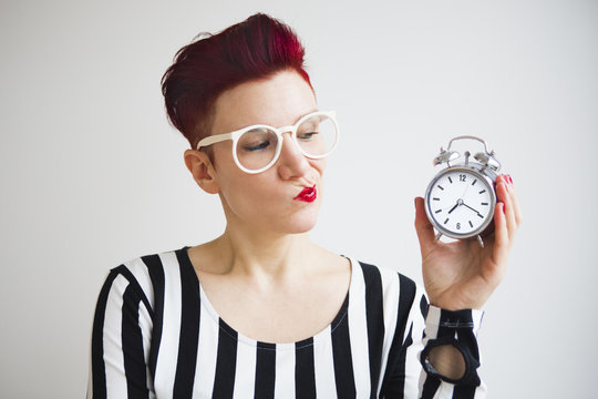 red-haired woman holding alarm clock looking upset