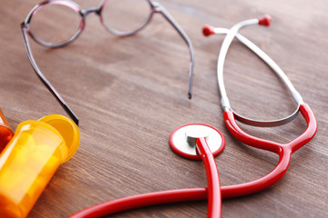 Medical stethoscope with bottles of pills on wooden table close up