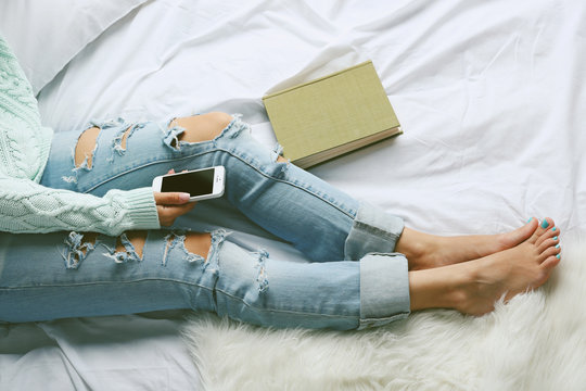 Woman in blue jeans watching phone on bed top view point