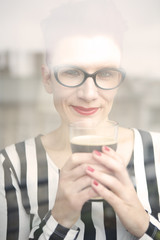 woman behind window holding a glass of coffee