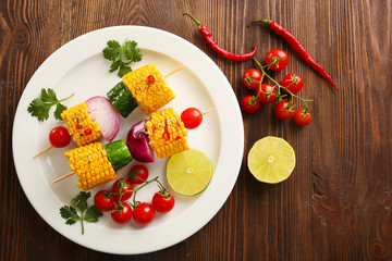 Delicious grilled corn and vegetables on white plate on wooden background