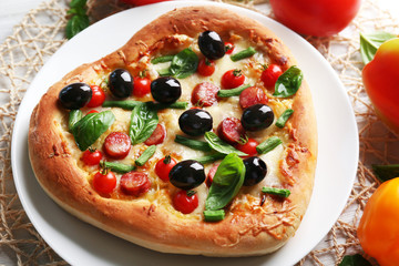 Delicious heart shaped pizza on the plate with vegetables around, close up