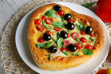 Delicious heart shaped pizza on the plate with vegetables around, close up