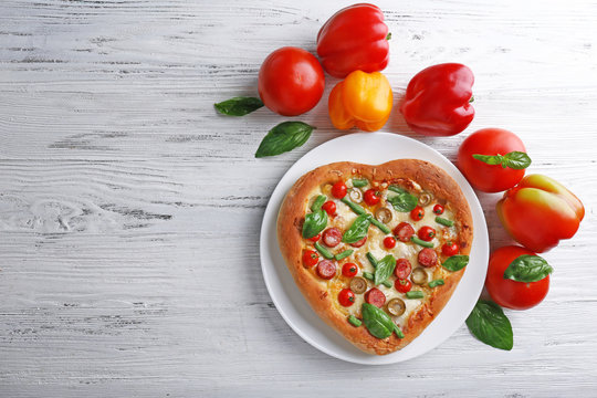 Delicious heart shaped pizza with vegetables on wooden background