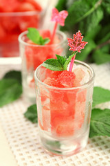 Cold watermelon pieces in glasses, on wooden table background