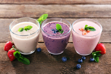 Tasty blueberry, strawberry and milk yogurts in a row decorated with berries and mint on wooden background