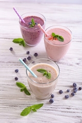 Fresh strawberry, blueberry and milk yogurts with mint and berries around on light wooden background