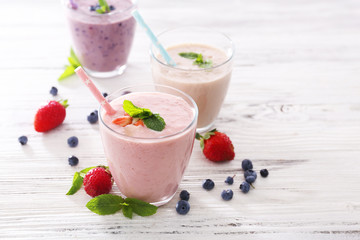 Fresh strawberry, blueberry and milk yogurts with mint and berries around on light wooden background