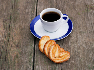 cup of coffee and three cookies in a row in front, on a wooden t