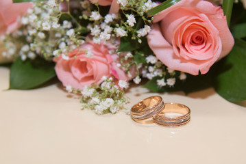 Two wedding rings lie the table.Beckett pink roses.