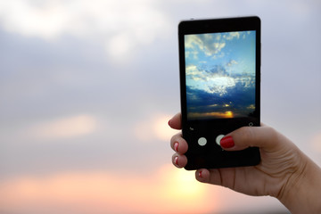 Woman using smart phone for taking photo of beautiful sky