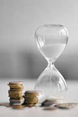 Hourglass with coins on table on bright background