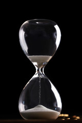 Hourglass and coins on wooden table on black background