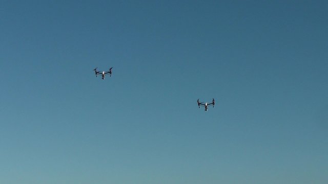 Two small surveillance camera drones hovering side by side against a clear blue sky