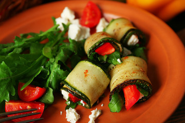 Zucchini rolls with cheese, bell peppers and arugula on plate, close-up, on table background