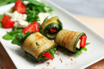 Zucchini rolls with cheese, bell peppers and arugula on plate, close-up, on table background