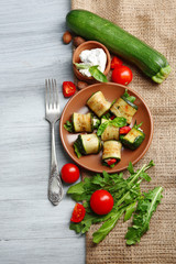 Salad with arugula and zucchini rolls on plate, on table background